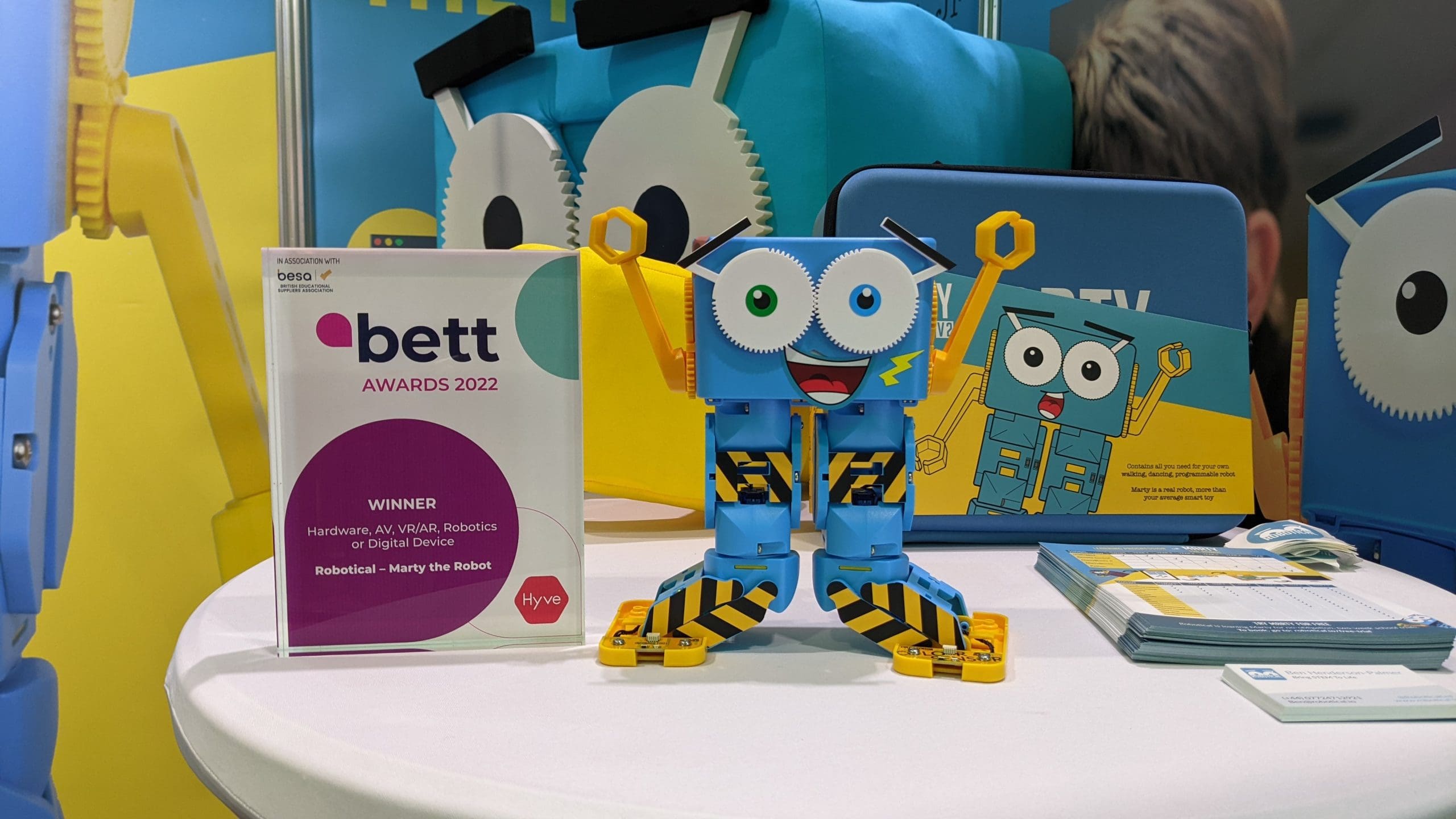 Celebratory Marty the robot standing next to bett awards trophy