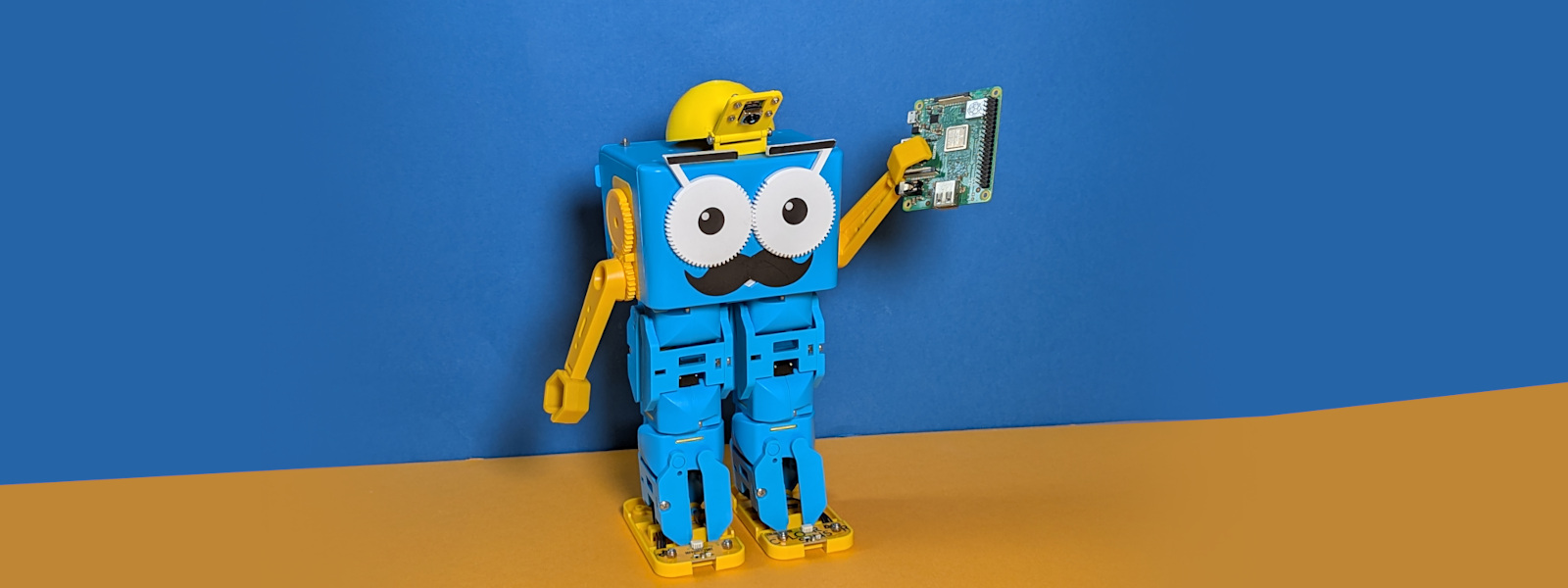 Marty the Robot with a camera hat, holding a Raspberry Pi